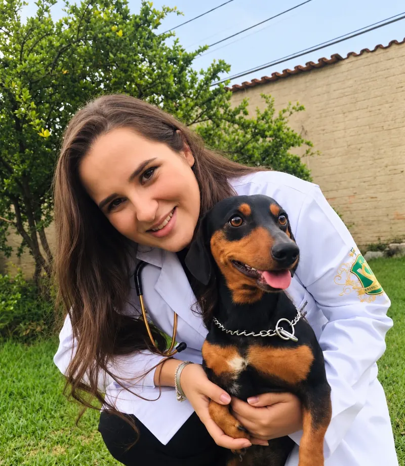 Dra. Gesielle Rangel de jaleco e estetoscópio, abraçando um cachorro preto e caramelo no jardim