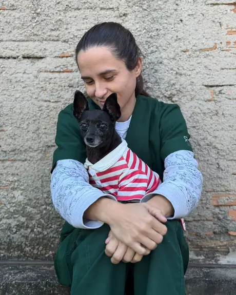 Veterinária de pijama verde com um cachorrinho preto de roupa listrada no colo