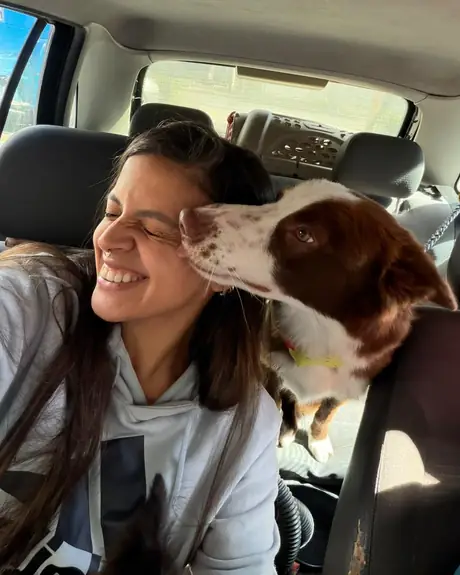 Veterinária sorrindo no carro com um cachorro marrom e branco apoiado no banco