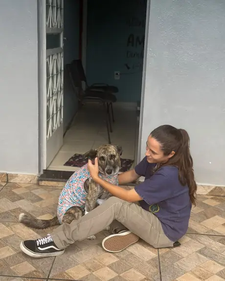 Veterinária sentada no chão com um cachorro de roupa cirúrgica na porta da clínica